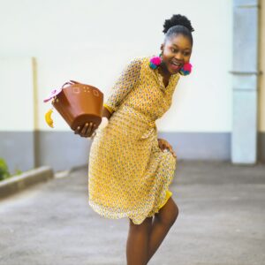 Chic woman in a yellow dress and colorful earrings posing outdoors, exuding joy and fashion-forward vibes.