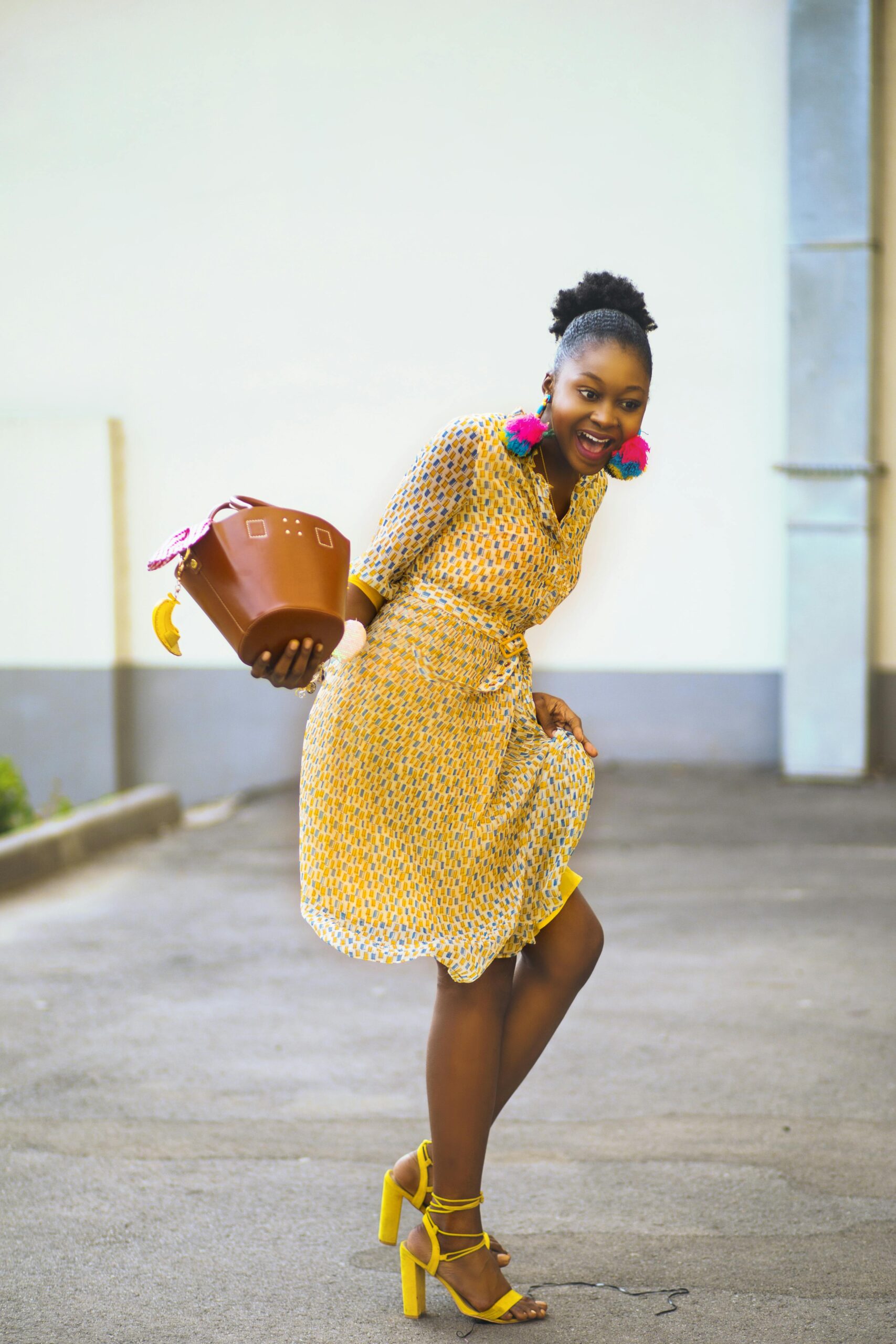 Chic woman in a yellow dress and colorful earrings posing outdoors, exuding joy and fashion-forward vibes.